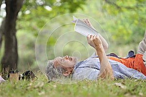 old mature male relax outside in nature garden,happy senior man smile,casual lying on his back on grass reading a book