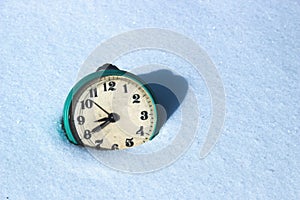 Old mechanical alarm clock lies in the snow.