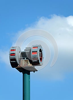 Old mechanical warning siren on a pole against a blue cloudy sky