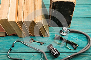 Old medical books with stethoscope, glasses, bottle and key on b