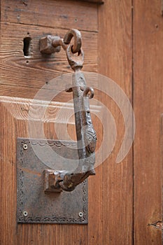 Old medieval metal handle on dark wooden door.