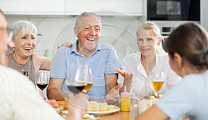 Old men and women talking merrily while having snack in the kitchen