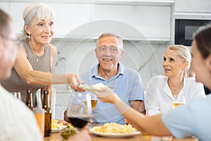 Old men and women talking merrily while having snack in the kitchen