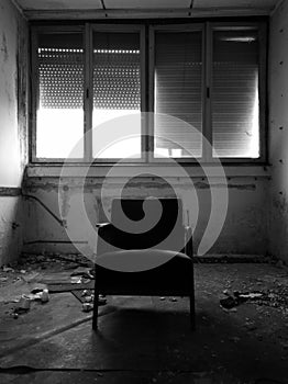 An old messy abandoned office with a dramatic atmosphere and with one chair in the middle and the shutters down on the windows