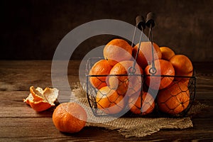 An old metal basket with fresh ripe tangerines and clementines on a wooden table