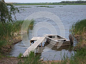 Old metal boat is tied at a wooden pier overlooking the river