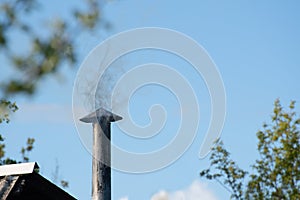 Old metal chimney with smoke against the blue sky