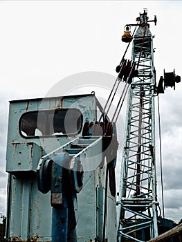 Old metal control cabin of a high large crane hauls scrap metal under blue sky