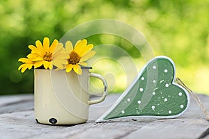 Old metal cup with flowers and a love symbol on a wooden table