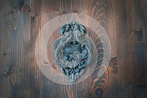 Old metal door handle knocker on a rough wooden background. Ancient door patina dark blue metal knocker of old family house.