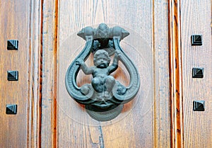 Old metal door knocker with a baby figurine on a wooden door