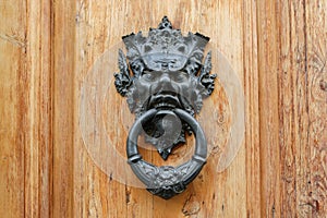 Old metal door knocker with satyrs head on a wooden door