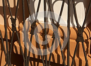 Old metal gate shadow on orange plaster wall.