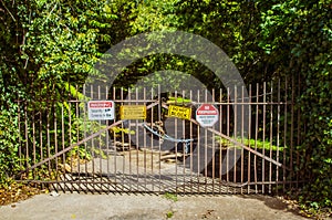 Old metal gate on shady road with chains and locks and signs saying no entry security cameras in use and no trespassing