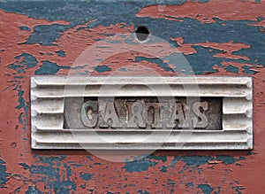 Old metal letterbox in a red wooden door with chipped peeling paint with the word cartas, translation from portuguese is mail