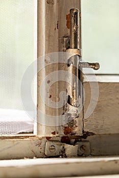 Old metal lock on a white wooden window frame. Old wooden window frame with a small rusty lock.