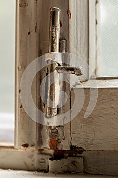 Old metal lock on a white wooden window frame. Old wooden window frame with a small rusty lock.