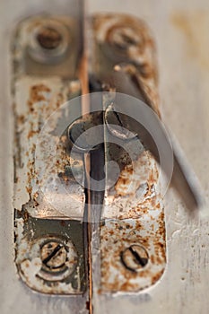 Old metal lock on a white wooden window frame. Old wooden window frame with a small rusty lock.