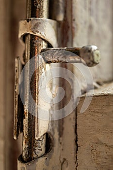 Old metal lock on a white wooden window frame. Old wooden window frame with a small rusty lock.