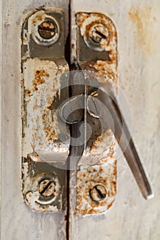 Old metal lock on a white wooden window frame. Old wooden window frame with a small rusty lock.