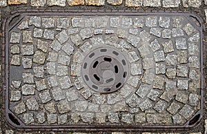 Old metal manhole cover on cobblestone street, Poland