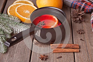 Old metal pan pot of tasty mulled wine with pot with spices and orange fruits on wooden table