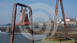 Old metal red fishing bell in harbour view of Fife Scotland village UK church in background