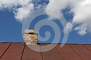 Old metal roof with brick chimney against cloudy sky.