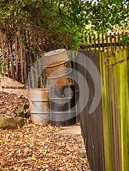 Old metal rusty barrels in the corner of a garden at a wooden fence