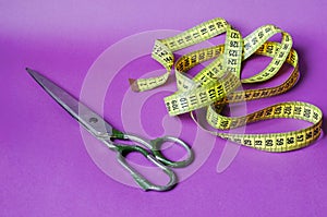 Old metal scissors and a yellow measuring tape on a purple background