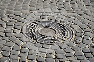 Old metal sewer hatch in the middle of the road, laid out of a smooth paving ston