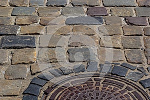 Old metal sewer hatch in the middle of the road, laid out of a smooth paving stone