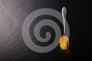 Old metal spoon with spices on a black background