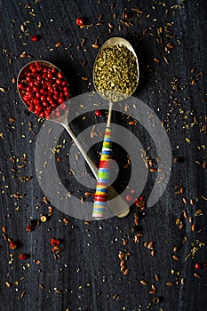 Old metal spoons with oregano and red peppercorn on black background