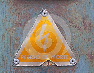 an old metal triangular yellow Portuguese electricity safety sign with a lightning bold symbol reading perigo de morte - photo