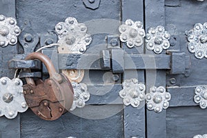 The old metal wrought-iron door is locked with a padlock. Closed metal lock.