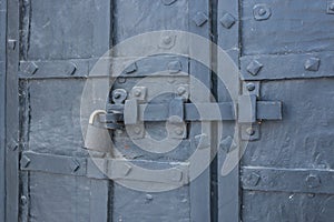 The old metal wrought-iron door is locked with a padlock. Closed metal lock.