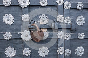 The old metal wrought-iron door is locked with a padlock. Closed metal lock.