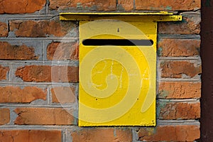 Old Metal yellow personal mailbox in a red brick wall.