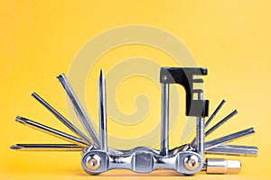 Old metallic bike multi tool set with chain remover on a yellow background. Bicycle multifunction hand tool