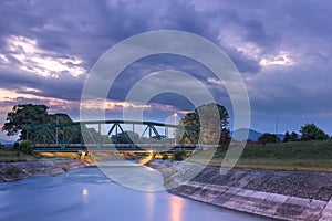 Old, metallic railroad bridge and river reflections during dramatic sunset