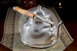 Old metallic teapot with wooden handle on an embroidered table mat