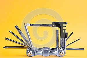 Old metallic unfold bike multi tool set with chain remover on a yellow background. Bicycle multifunction tool.