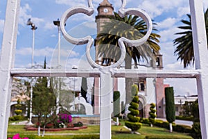 Old Mexican church, bushes, and palm trees from behind white fence