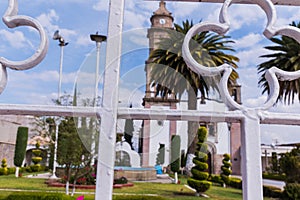 Old Mexican church, bushes, and palm trees from behind white fence