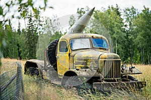 Old military equipment. Abandoned rusty yellow heavy war truck with big missile on board stands near the fence in an