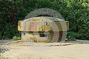 Old military green rusty iron tower with embrasures on a gray concrete pillbox