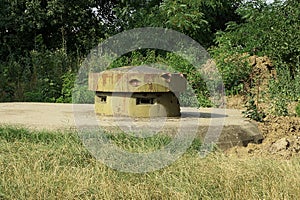 Old military green rusty iron tower with embrasures on a gray concrete pillbox