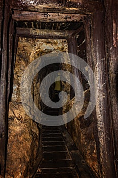 Old mine shaft with wooden timbering and person dressed in a mining mantel in background