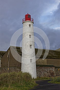 The Old Montrose Rear Lighthouse hidden down a small street at the Port of Montrose, with dark clouds above.